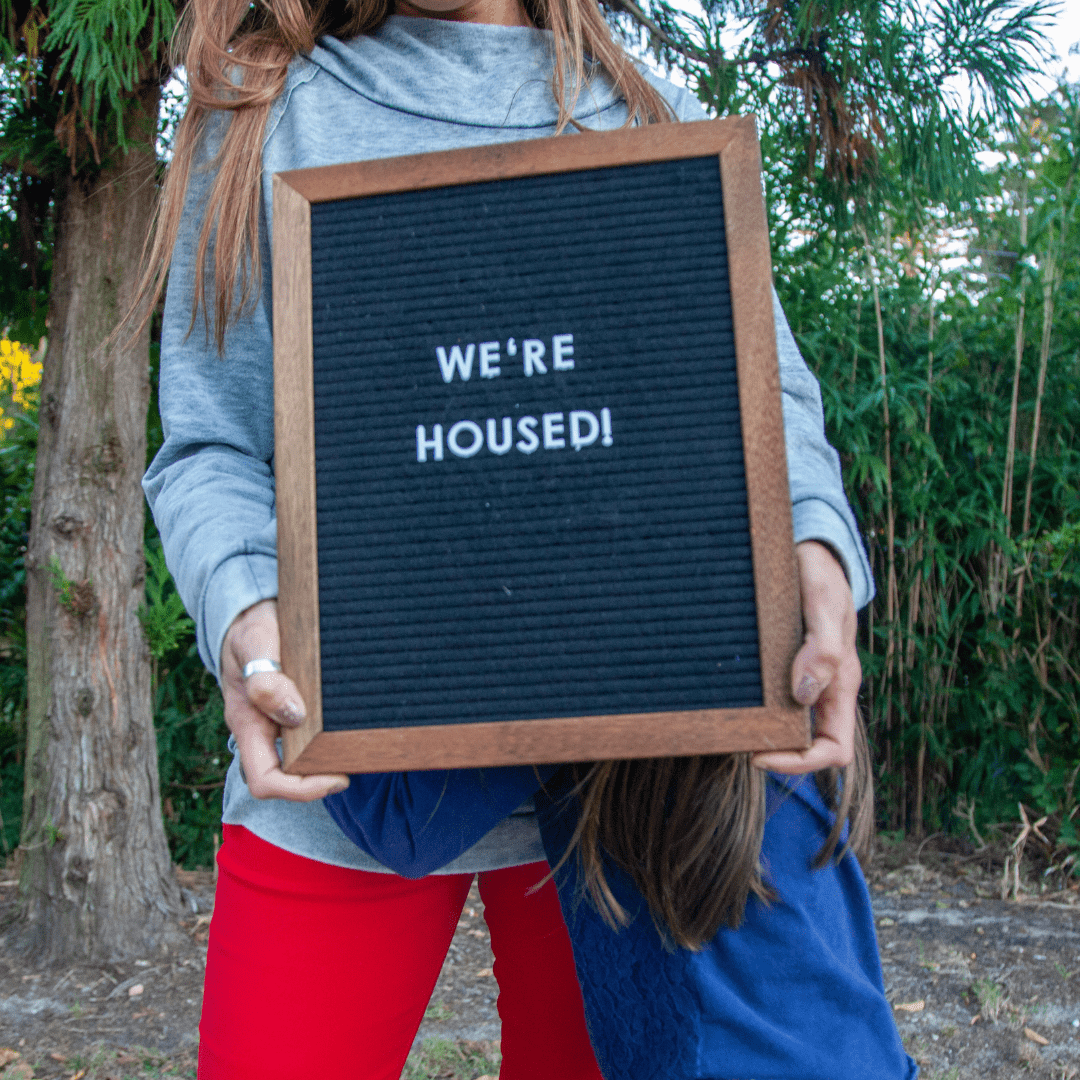Client holding a letter board that says We’re housed!